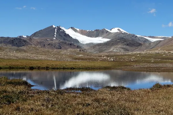 Schneebedeckte Gipfel spiegeln sich in einem Bergsee auf der kirgisischen Hochebene